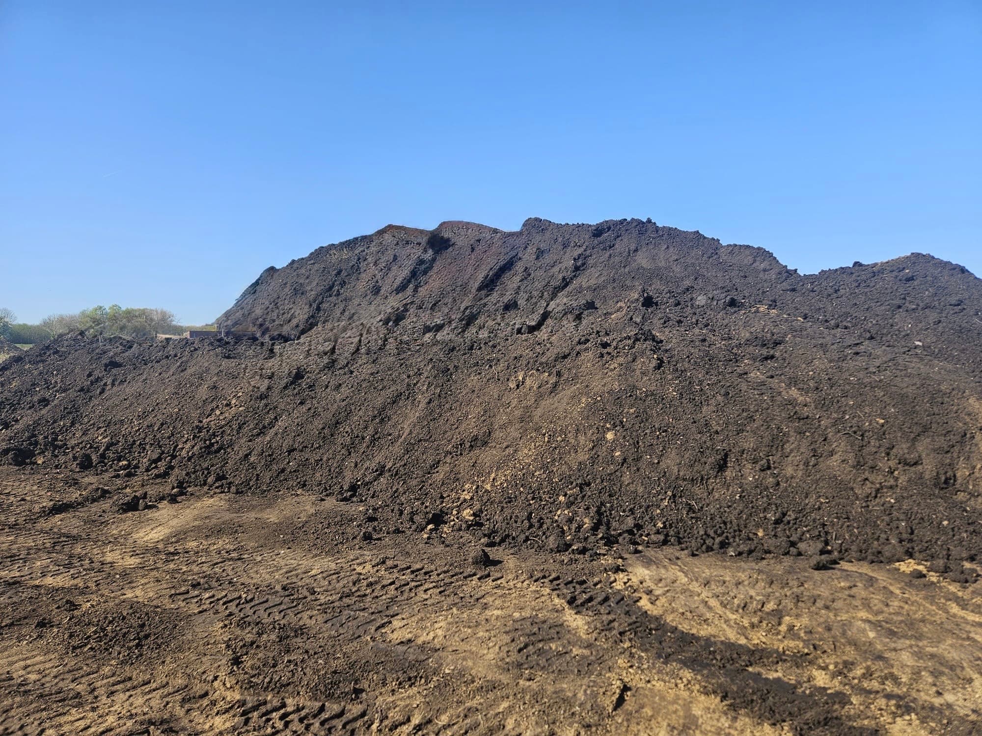 Grote berg donkere grond op een werf, met bandensporen ervoor