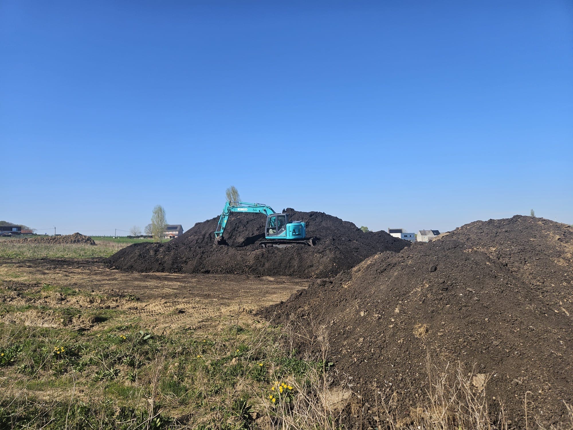 Graafkraan bovenop een opgehoogde grondberg naast een weiland